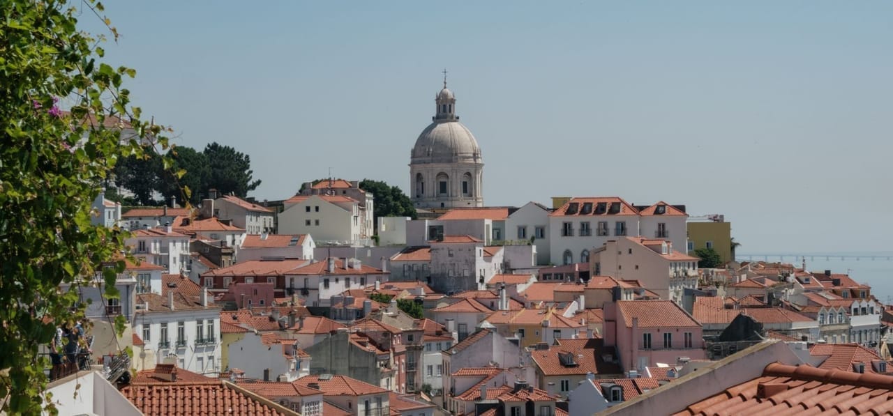 Lisbon's Alfama district at golden hour, warm terracotta rooftops cascading down to the Tagus river, Castelo São Jorge silhouetted on the hill